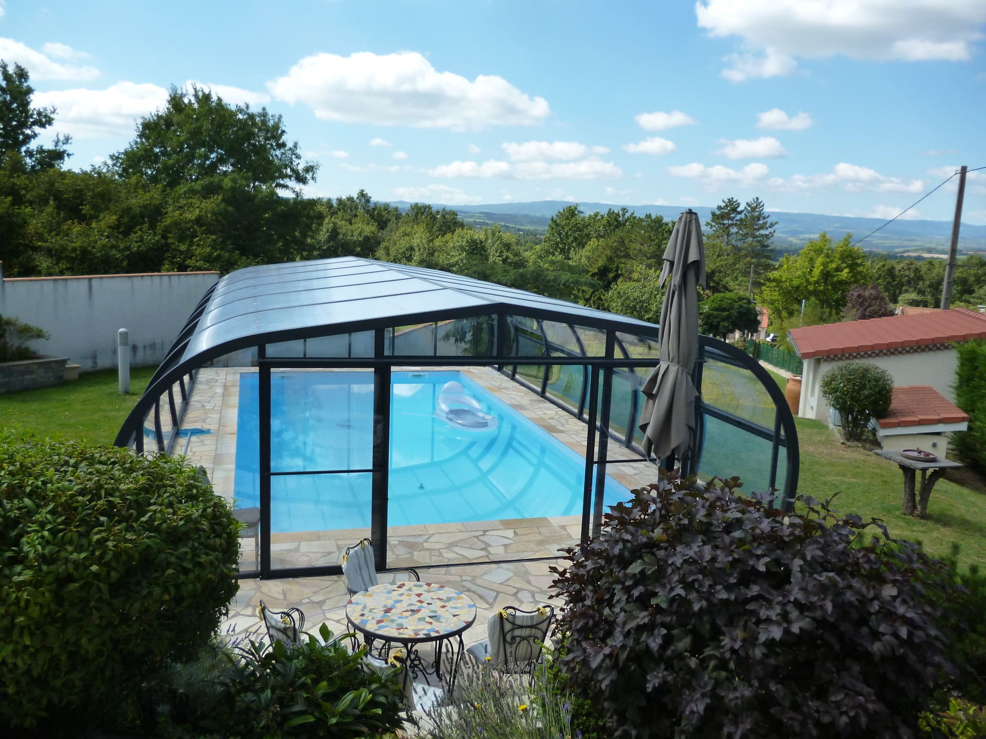 Abri HERA, avec façade avec porte double coulissante, surplombant une piscine coque installée par Art & Loisirs Piscines à Peltre. 